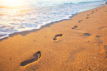 beach, wave and footprints at sunset time