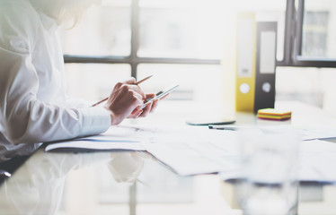 Young businesswoman working new startup project modern office.Contemporary smartphone holding female hands and texting message. Analyze, statistics plans table.Horizontal, film effect. Blurred 