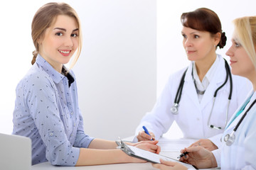 Happy smiling female patient with two cheerful doctors in the background. Medical and health care concept