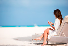 Young Woman On Lounger With Mobile Phone At The Beach