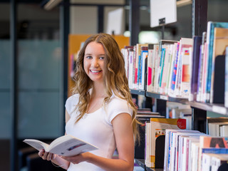 Wall Mural - Happy female student holding books at the library