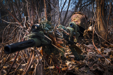 Sniper wearing camouflage suit with rifle hide in the woods