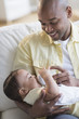 © JGI/Tom Grill/Blend Images - Smiling father feeding baby on sofa