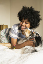 Mixed Race Woman Playing With Dog On Bed