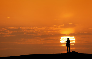 Wall Mural - sunset landscape with silhouette of a standing man on the background of solar disk and colorful yell