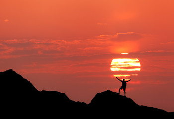 Wall Mural - sunset landscape with silhouette of a standing happy man with backpack and raised-up arms on the bac