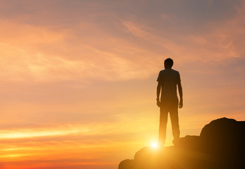 Wall Mural - landscape with silhouette of a standing man on the background of colorful yellow sky on the rock at 