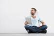 © Westend61 - Portrait of young man sitting on floor holding tablet computer