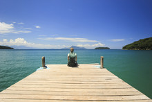 Traveller Sitting On Pier In Ocean Beach With Green Water