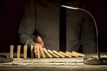 Front view of businessman stopping falling dominos with his hand