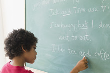 Mixed Race Boy Writing On Chalkboard In Grammar Lesson