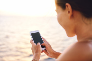 Smartphone woman texting on social media app looking at display screen for sms reading on ocean background on a sea cruise balcony or beach at sunset on holiday. Unrecognizable girl using smart phone.