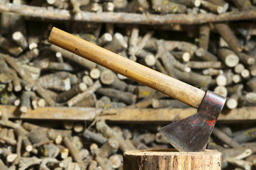 old axe , hatchet , in stump with unfocused  firewood background