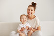 © WHstudio Leushin N - Charming brunette woman playing with her baby while sitting on a bed in her apartment at the weekend together, lazy morning, warm and cozy scene. Selective focus