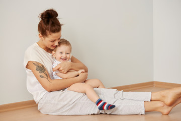 Mother and child on a white bed. Mom and baby boy in diaper playing in sunny bedroom. Parent and little kid relaxing at home. Family having fun together at the weekend together. Selective focus