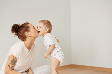 Mother and child on a white bed. Mom and baby boy in diaper playing in sunny bedroom. Parent and little kid relaxing at home. Family having fun together at the weekend together. Selective focus