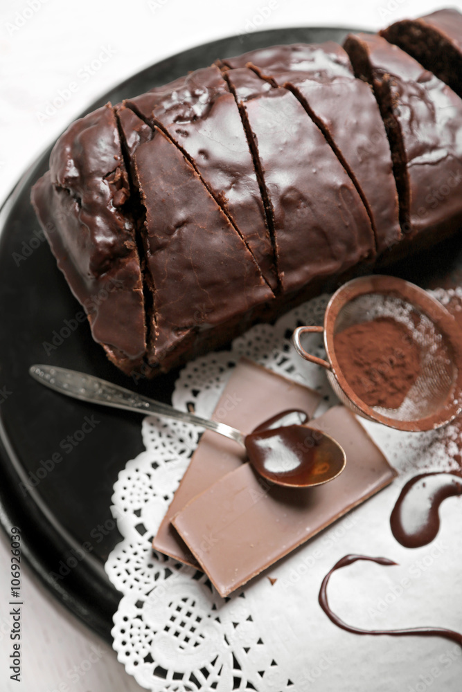 Chocolate sliced cake with icing and cocoa powder on baking dish over white table