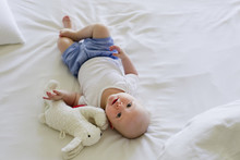 Baby Girl Lying On Bedclothes With Soft Toy