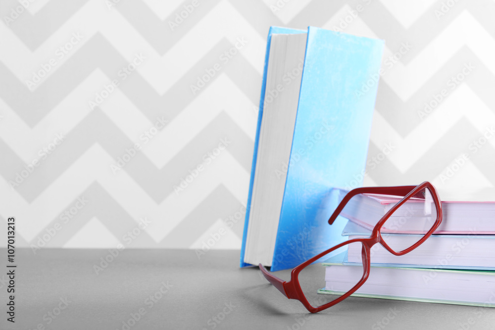 Books and eyeglasses on grey table against ornament wall, close up