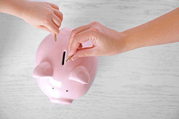 Canvas Print - Savings concept. Hand putting coin in the piggy bank on wooden background