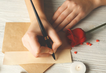 Wall Mural - Female hands signing gift card for Valentine's Day on white wooden background