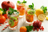 Fototapeta Kuchnia - Refreshing cocktails with ice, mint, pomegranate seeds and slices of fruits on light wooden background