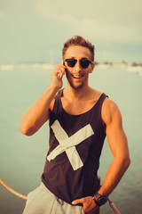 Wall Mural - young guy in sunglasses t-shirt talking on the smartphone to respond to messages texting working abroad,freelance working,typing online,social networks,periscope,wi-fi ,hand watch 