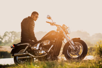 young brutal man in a black jacket and glasses standing near a motorcycle