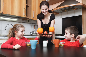 yooung mother give orange fruits to her daughter and son in the kitchen