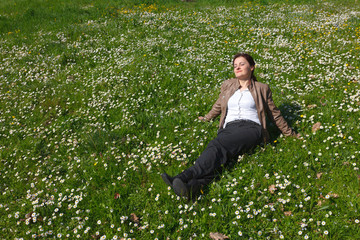 Relaxing young woman in pants and leather jacket enjoying spring, lying on grass and spring flowers