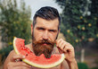 © endrews21 - bearded man without clothes with a big juicy ripe watermelon in hands on a background of flowering garden illuminated by bright sunshine