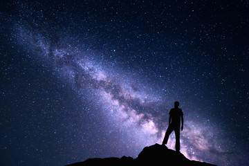 Wall Mural - landscape with purple milky way. night sky with stars and silhouette of a happy man on the stone. be