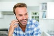 © WavebreakmediaMicro - Happy handsome man talking on cellphone in kitchen