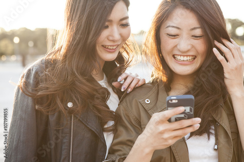 Fotografia, Obraz Two young women are laughing to see the smartphone