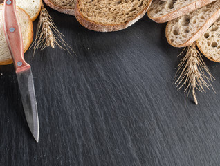 Wall Mural - Bread slices, a wheat and a knife on the black stone desk.