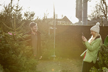 A Man And Woman Choosing A Traditional Pine Tree, Christmas Tree From A Large Selection At A Garden Centre.  
