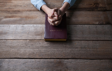 Wall Mural - hands praying with a bible in a dark over wooden table