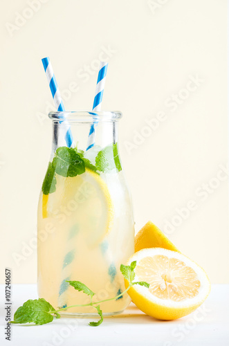 Fotografía Bottle of homemade lemonade with mint, ice, lemons, paper straws and pastel blue