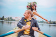 © nataliakabliuk - bride and groom sitting in an orange row boat floating out of the tree covering and in to the lake. Bride with wreath of flowers