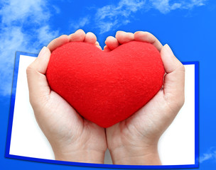 Red heart symbol on hands blue sky background