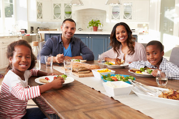 Wall Mural - Parents and children eating at kitchen table look to camera