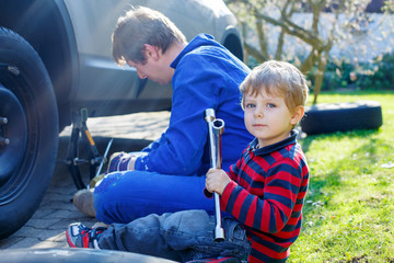 Little kid boy and his father changing wheel on car 