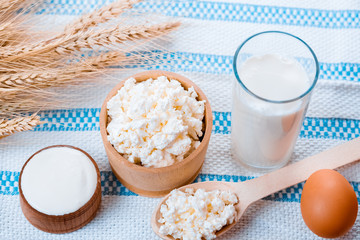 Cottage cheese, glass of milk, two eggs, wooden spoon with cottage cheese and wheat ears lie on the napkin from a burlap on the old wooden table