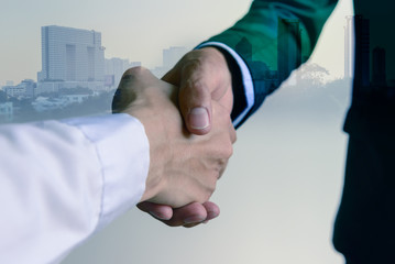 Double exposure closeup of businessman handshake with cityscape background.