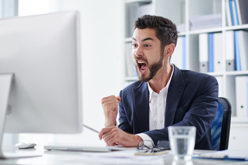 Happy young entrepreneur screaming of joy when looking at computer screen