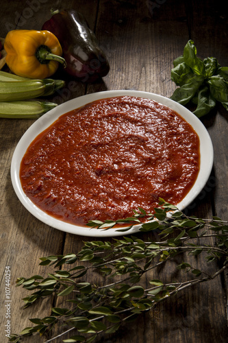 Fotografía piatto di salsa al pomodoro in mezzo a vari ortaggi su un tavolo in legno