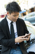 © Rick Gomez/Blend Images - Korean businessman using cell phone near car
