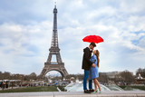 Fototapeta Paryż - beautiful couple with umbrella near Eiffel Tower, honeymoon in Paris, romantic moment