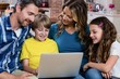 © WavebreakMediaMicro - Parents and kids sitting on sofa and using a laptop