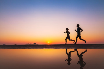 Wall Mural - workout, silhouettes of two runners on the beach at sunset, sport and healthy lifestyle background